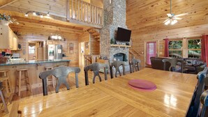 A spacious wooden cabin with a large dining table, stone fireplace, and a balcony overlooking the forest. - Forested Hideaway, Sleeps 14・Hot Tub・Pool Access (Sevierville)