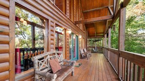 A wooden cabin with a covered porch, wooden benches, and a view of the surrounding forest. - Forested Hideaway, Sleeps 14・Hot Tub・Pool Access (Sevierville)