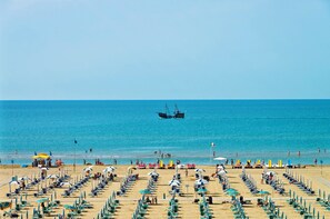 Een strand met rijen ligbedden en parasols, een heldere blauwe zee en een vissersboot in de verte.