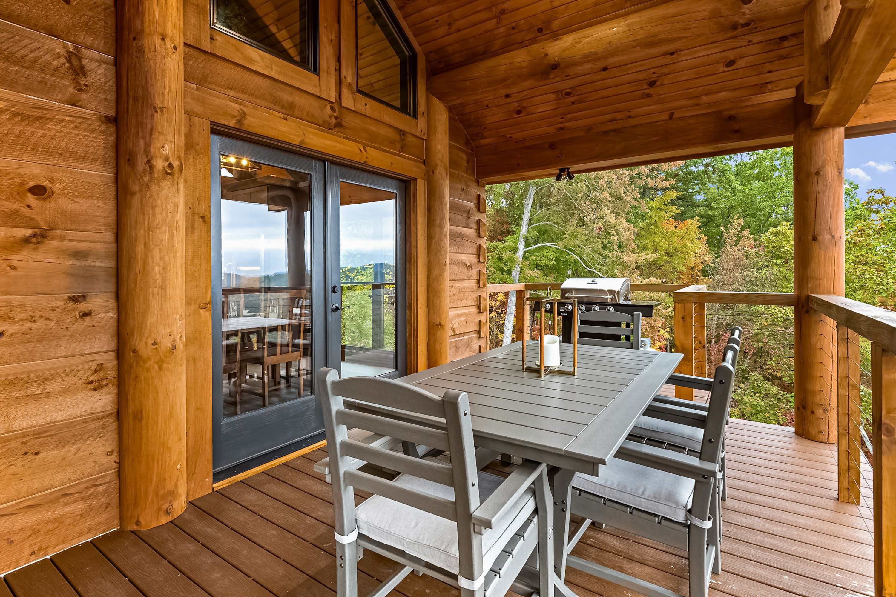 A wooden deck with a table and chairs, a grill, and a view of trees and hills.