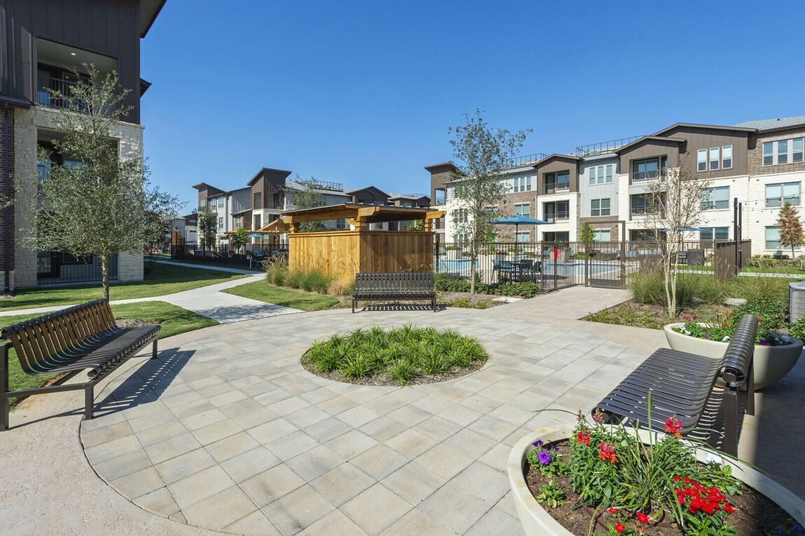 A courtyard with benches, a wooden structure, and a pool area surrounded by modern buildings.