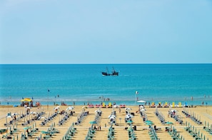 A beach with rows of sun loungers and umbrellas, a clear blue sea, and a fishing boat in the distance. - Bia's Beach Residence: Two-Room Bilo D3 Apartment for 5 People (Bibione)