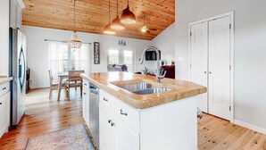 Eine moderne Küche mit Holzboden, weißen Schränken, einer zentralen Kochinsel mit Spüle und Pendelleuchten.