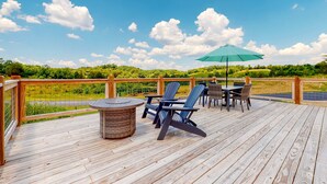 Eine Holzterrasse mit Gartenmöbeln, darunter Stühle und ein Tisch, und einem grünen Sonnenschirm.