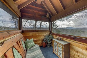 A cozy cabin interior with a wooden bench, a small cabinet, and a large window offering a view of trees and mountains. - Cozy Cabin W Wooded View, Sleeps 6・Near Downtown (Sevierville)