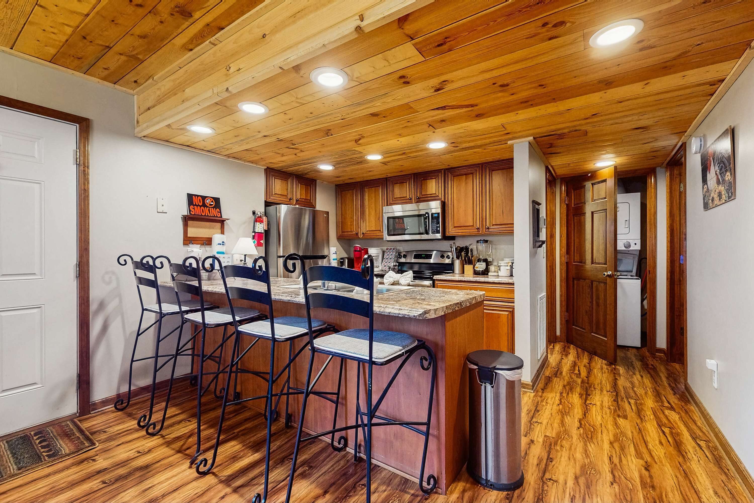 Cocina con techo de madera, electrodomésticos de acero inoxidable y una zona de bar con sillas de metal.