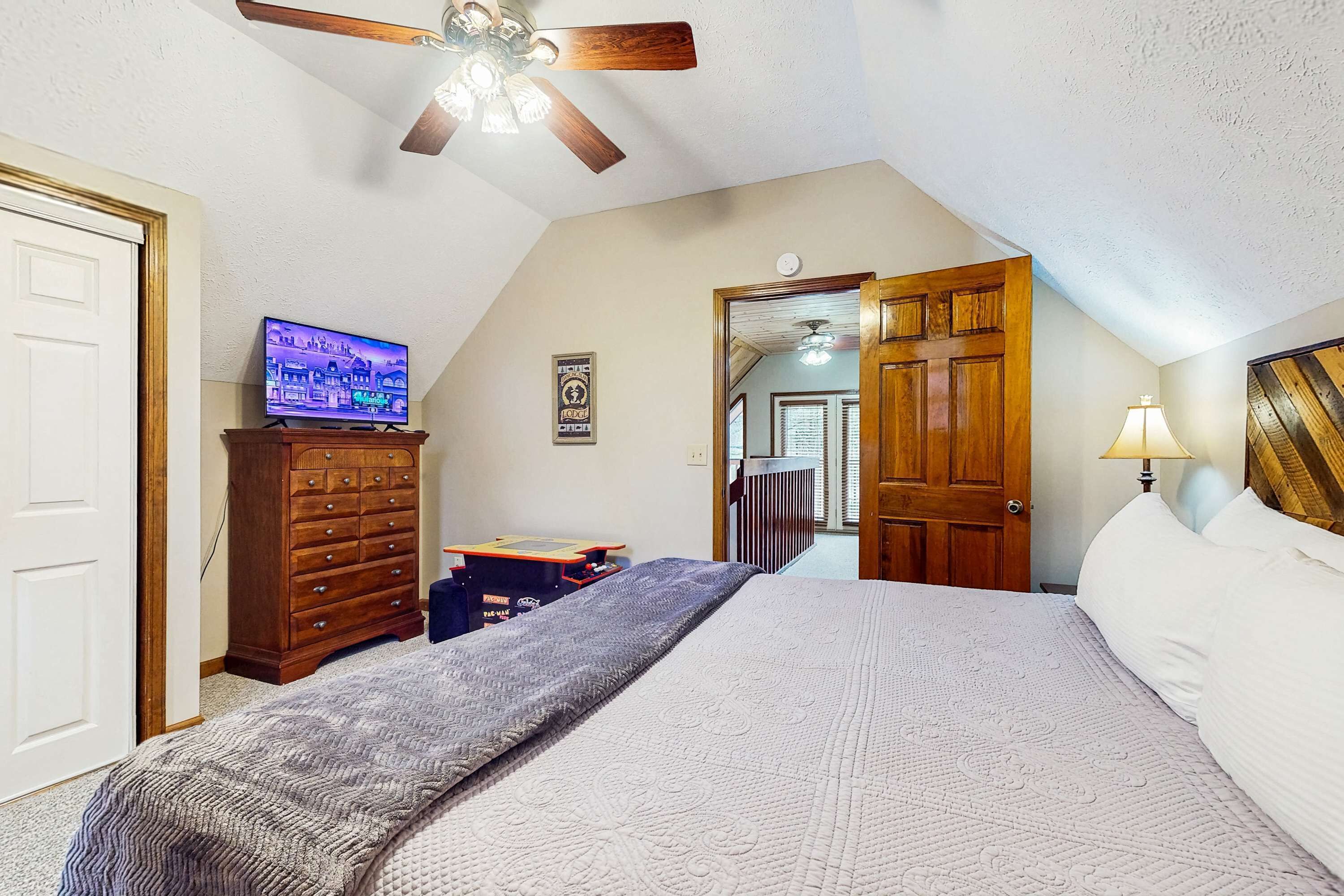 A bedroom with a bed, a dresser, a television, and a ceiling fan.