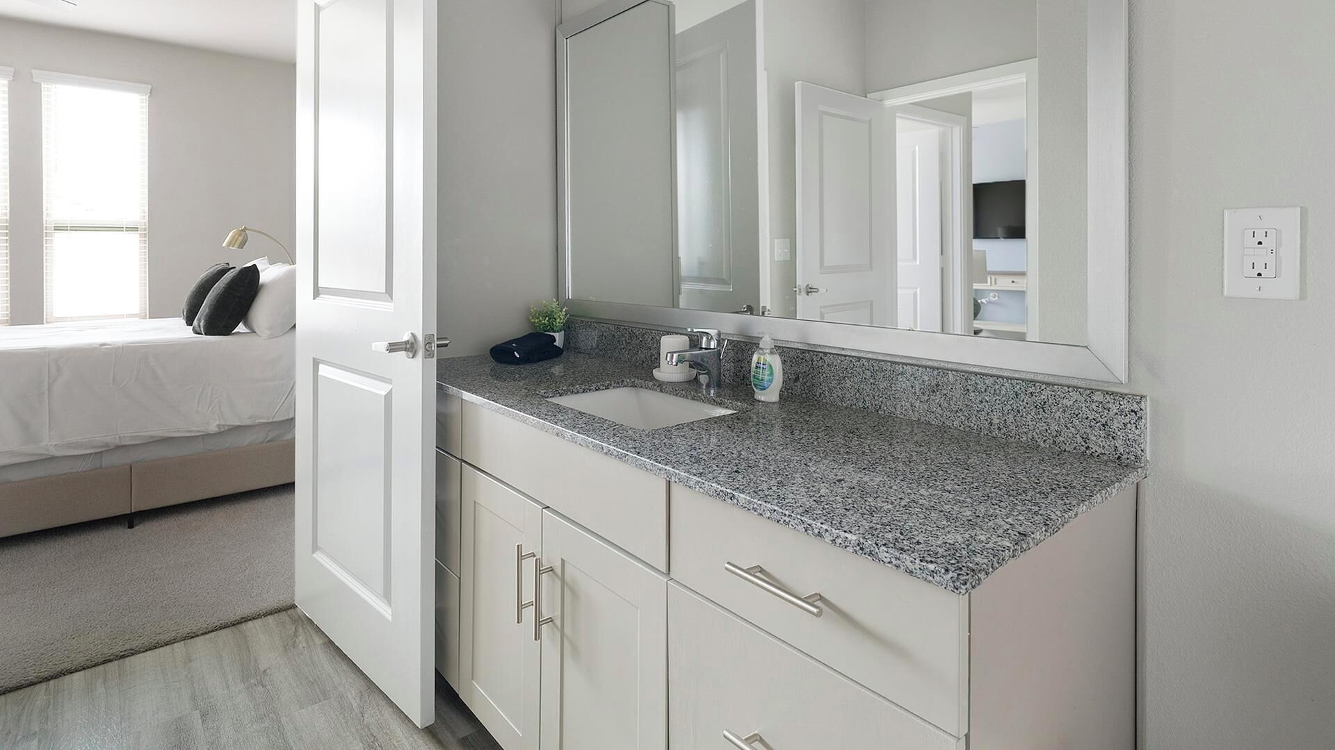 Une salle de bain moderne avec un comptoir en granit, un lavabo blanc et un grand miroir.