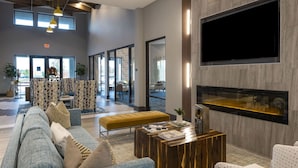 A modern hotel lobby with a large flat-screen TV, a wooden coffee table, and a seating area with a sofa and armchairs. - Landing | Amazing 2BD, Gym, Pool (Katy)