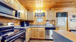 A kitchen with wooden cabinets, a stainless steel oven, a dishwasher, and a granite countertop. - Homey Cabin W Hot Tub・2 Porches・Pool Table・Games (Pigeon Forge)