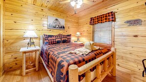 A cozy wooden cabin room with a bed, two bedside lamps, a ceiling fan, and a window with blinds. - Homey Cabin W Hot Tub・2 Porches・Pool Table・Games (Pigeon Forge)
