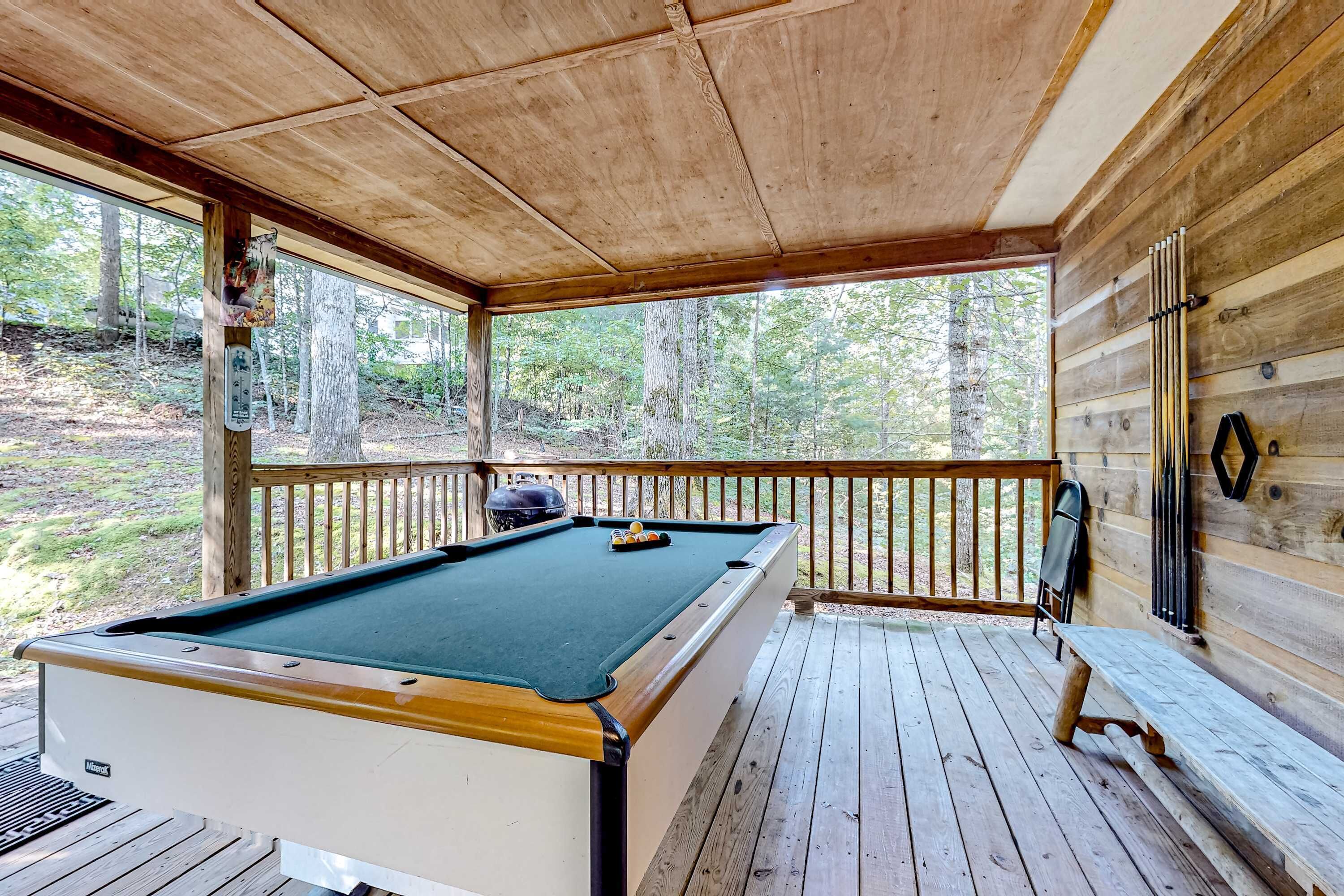 Une table de billard se trouve dans un espace extérieur abrité, doté d’une terrasse en bois et d’une rambarde.