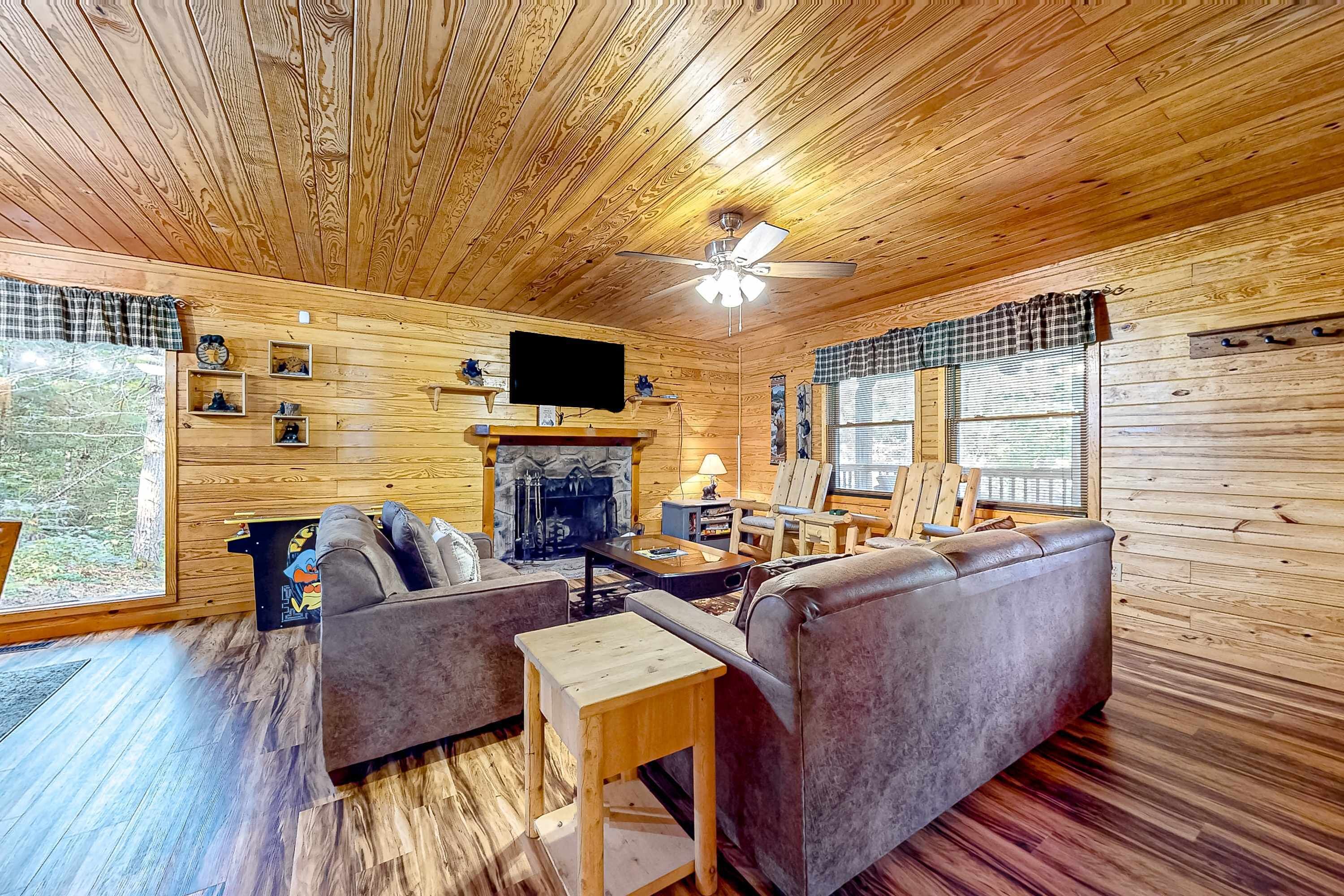 A cozy cabin interior with wooden walls, a fireplace, a sofa, and a television.