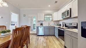 Una cocina moderna con armarios blancos, electrodomésticos de acero inoxidable y una mesa de comedor de madera con sillas.