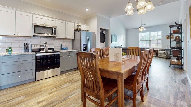 Una cocina moderna con electrodomésticos de acero inoxidable, un comedor con sillas de madera y vista al salón.