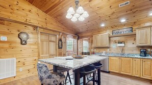 A wooden cabin interior with a kitchen area featuring a large island, bar stools, and wooden cabinets. - Tranquil Cabin W Hot Tub・Boat / Motorcycle Parking (Sevierville)