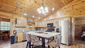 A wooden cabin-style kitchen with a central island, bar stools, a refrigerator, a microwave, and wooden cabinets. - Tranquil Cabin W Hot Tub・Boat / Motorcycle Parking (Sevierville)