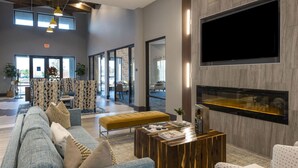 Eine moderne Hotelhalle mit einem großen Flachbildfernseher, einem Holztisch und einer Sitzecke inklusive Sofa und Sesseln.