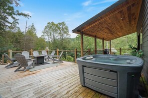 Ett trädäck med Adirondack-stolar, en bubbelpool och ett takförsett område med utsikt över den omgivande skogen.
