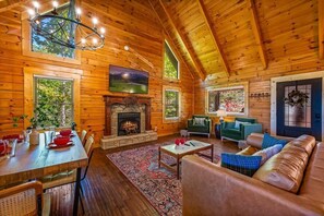 A cozy log cabin interior with a fireplace, wooden walls, a dining area, and a living room with a sofa and a TV. - Charming Log Cabin, Sleeps 8・Hot Tub・Arcade, Views (Sevierville)