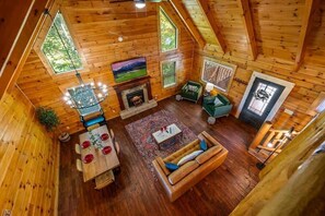 A cozy log cabin interior with a dining area, a fireplace, a sofa, and a staircase. - Charming Log Cabin, Sleeps 8・Hot Tub・Arcade, Views (Sevierville)