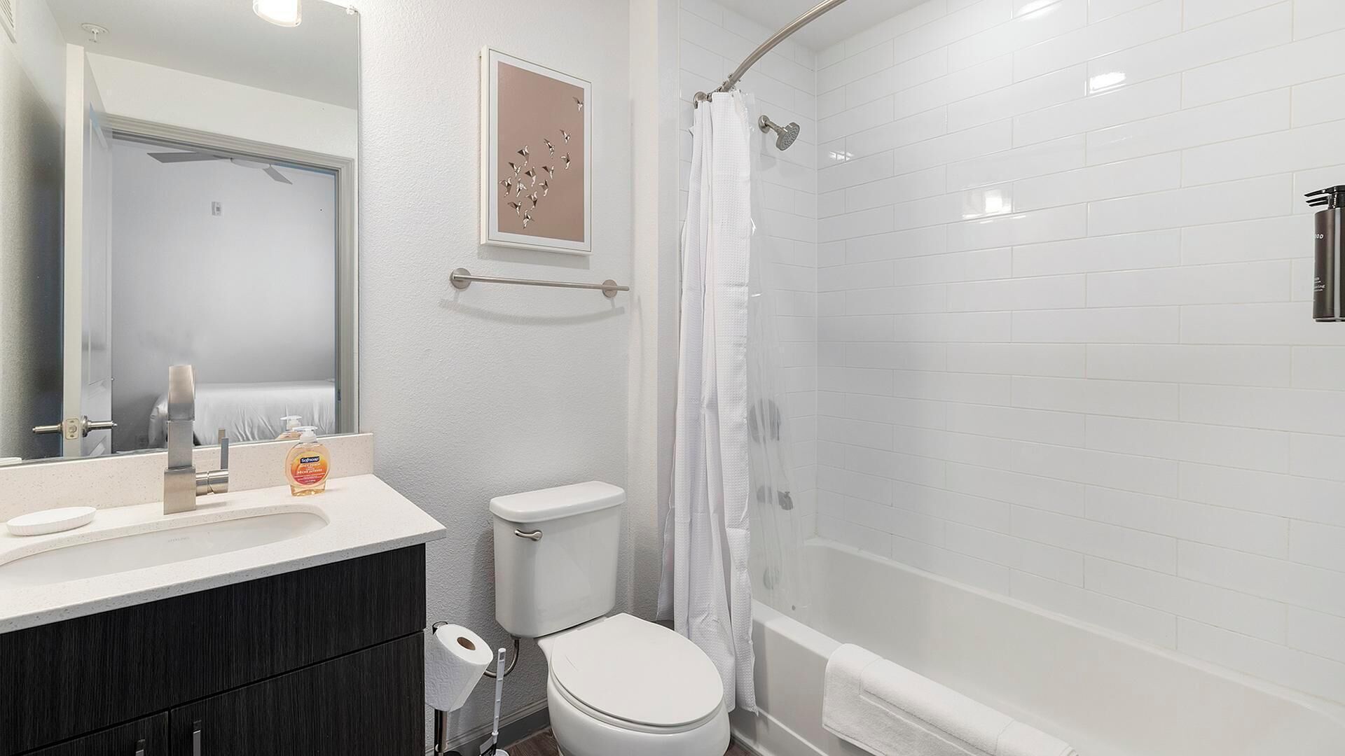 A modern bathroom with a white toilet, a shower with a glass door, and a vanity with a mirror and soap dispenser.