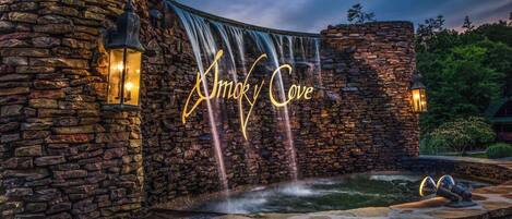 A stone building with a waterfall feature and the name "Amok Cove" illuminated on the wall.