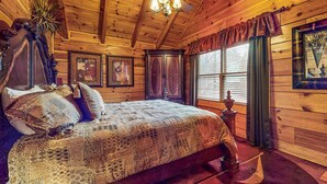 Un dormitorio de cabaña de madera con una cama grande, un ventilador de techo y una ventana con cortinas.