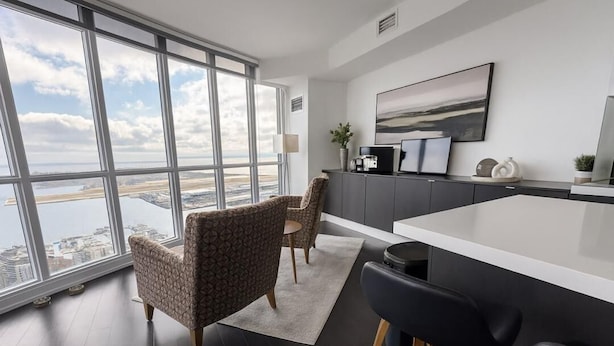 A modern kitchen with a large window, a dining area with patterned chairs, and a view of a body of water. - Iceboat Elegance Suites (Toronto)