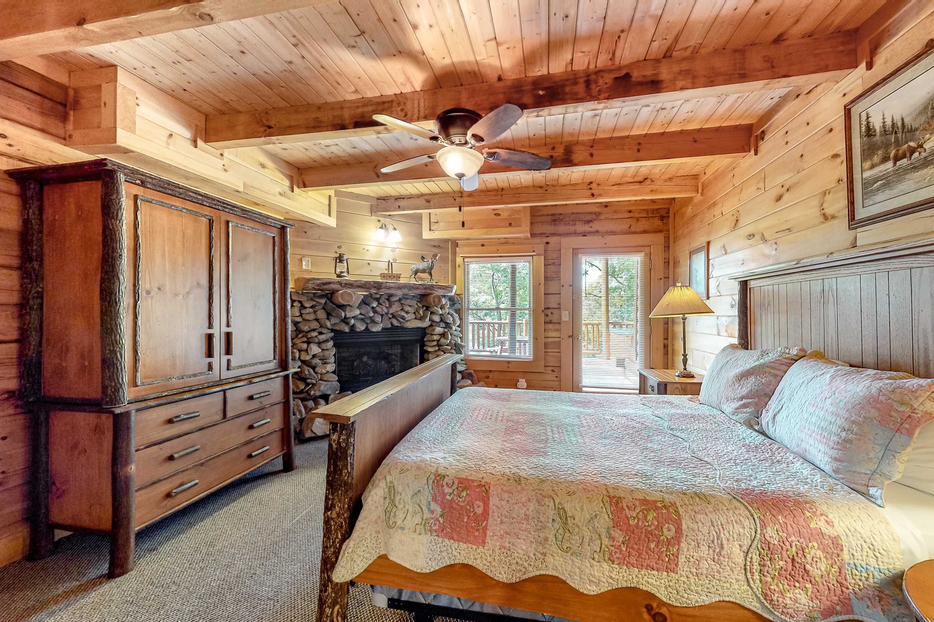 Camera da letto in baita di legno con un letto, un armadio in legno, un camino in pietra e una ventola a soffitto.