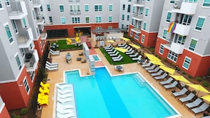 A rooftop pool area with multiple lounge chairs and umbrellas, surrounded by apartment buildings. - Landing | Stunning 2BD, Clubhouse, Gym (Arlington)