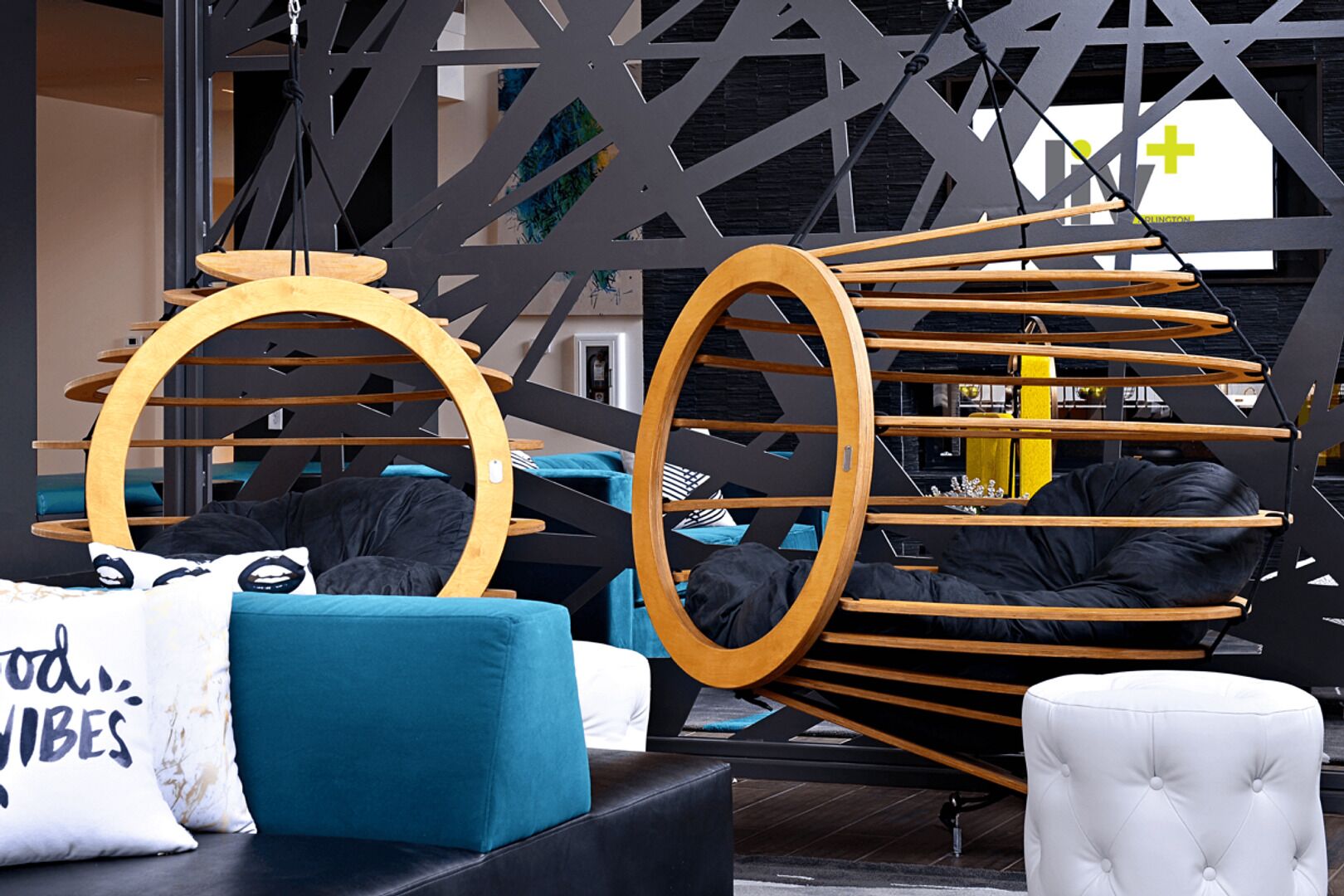 A modern interior with a circular wooden structure, a tufted ottoman, and a sofa with teal cushions.