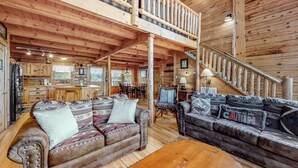 A spacious cabin interior with a high ceiling, wooden floors, a central seating area with two sofas, a dining area, and a kitchen. - Charming Dog Friendly Cabin・Hot Tub・Scenic View (Sevierville)