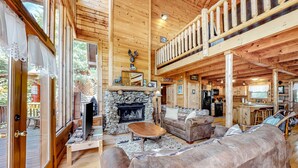 A cozy log cabin interior with a stone fireplace, wooden furniture, and a balcony. - Charming Dog Friendly Cabin・Hot Tub・Scenic View (Sevierville)