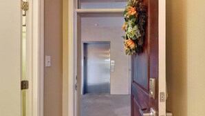 Entrada de hotel con puerta de madera, dispositivo de seguridad en la pared y decoración floral.