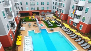 Un espace piscine aménagé sur le toit, doté de plusieurs chaises longues et de parasols, et entouré d’immeubles d’habitation.