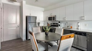 Une cuisine moderne avec des meubles blancs, des appareils en acier inoxydable et un coin repas comprenant une table ronde et des chaises.
