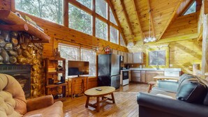 A cabin interior with a stone fireplace, wooden furniture, a kitchen area, and large windows. - 5 Mi to Pigeon Forge・Cozy Escape・Dog Welcome・Views (Sevierville)