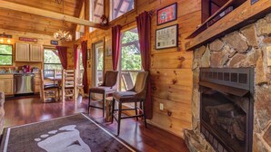 A wooden cabin interior with a stone fireplace, wooden dining table, chairs, and a kitchen area. - 8.6 Mi to Dollywood・Serene Cabin Getaway・Hot Tub (Sevierville)