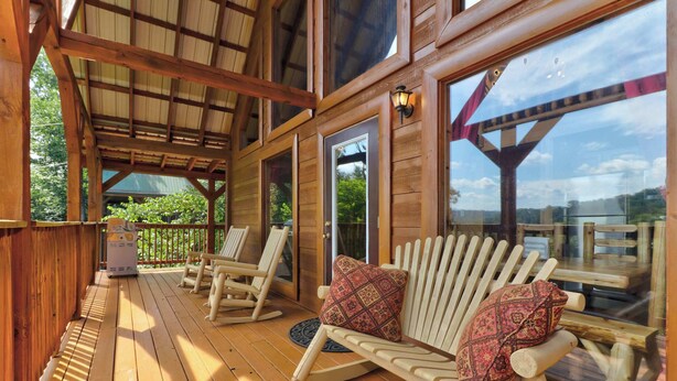 A wooden deck with rocking chairs and a bench, large windows, and a covered area with a view of the outdoors. - 8.6 Mi to Dollywood・Serene Cabin Getaway・Hot Tub (Sevierville)