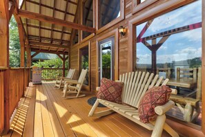 A wooden deck with rocking chairs and a bench, large windows, and a covered area with a view of the outdoors. - 8.6 Mi to Dollywood・Serene Cabin Getaway・Hot Tub (Sevierville)
