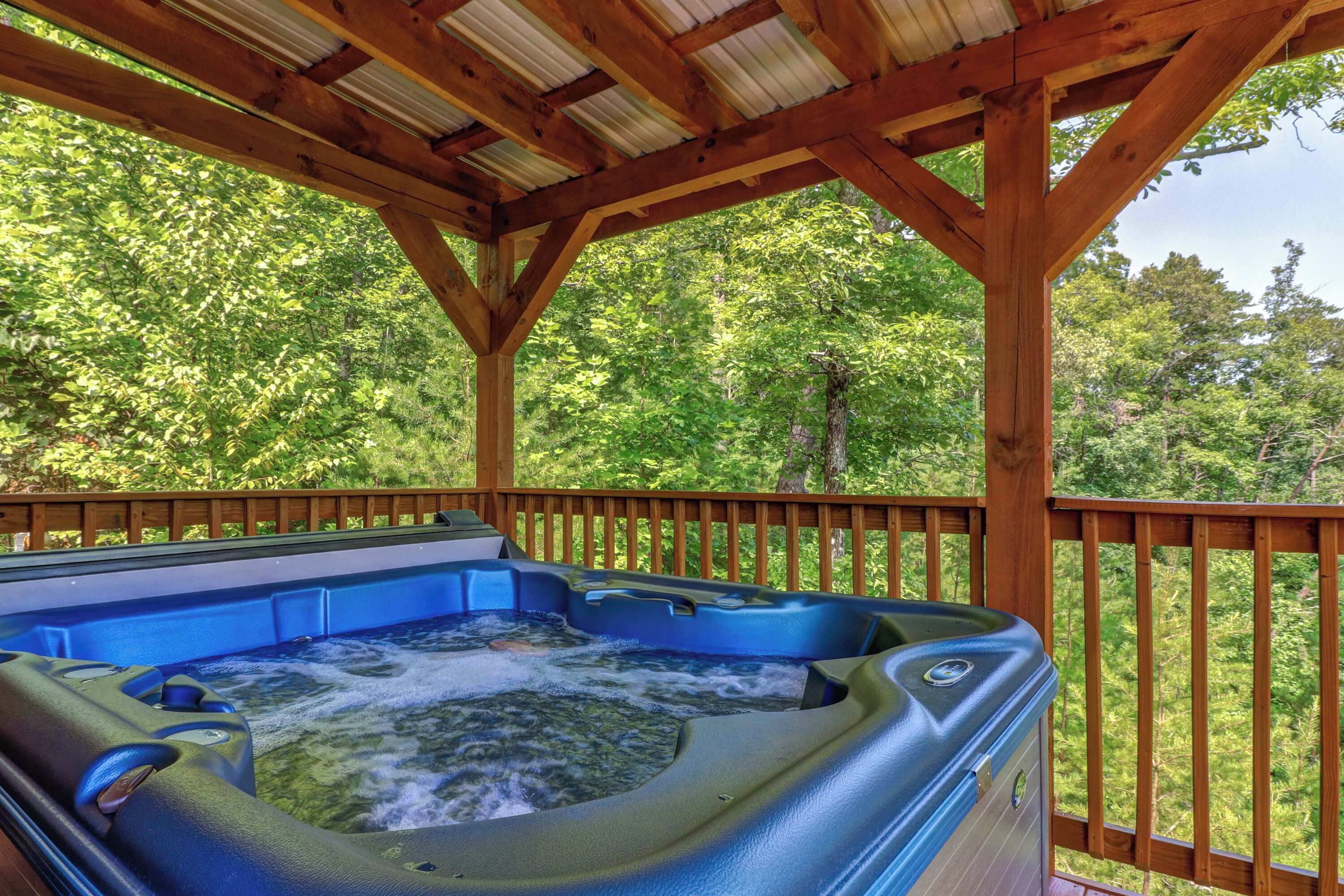A hot tub under a wooden pergola with a view of a forested area.