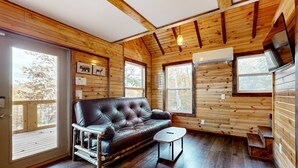 L’intérieur chaleureux d’un chalet avec un canapé en cuir, une petite table, des murs en bois et de grandes fenêtres.