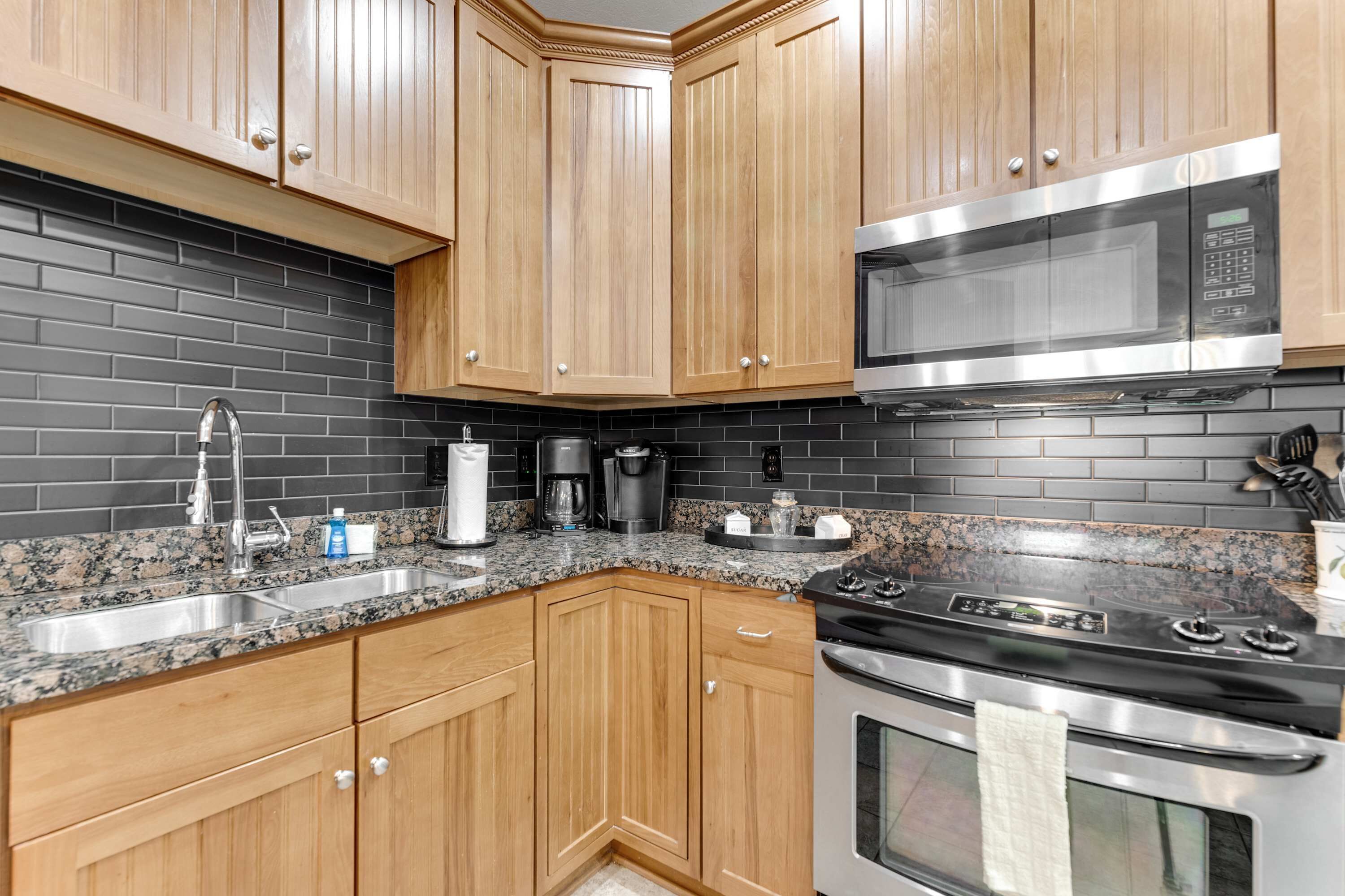 Una cocina con armarios de madera, encimera de granito, microondas de acero inoxidable y estufa.