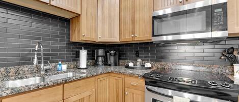 Una cocina con armarios de madera, encimera de granito, microondas de acero inoxidable y estufa.