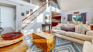 Un salón comedor amplio con techo alto, una escalera y vistas al exterior.
