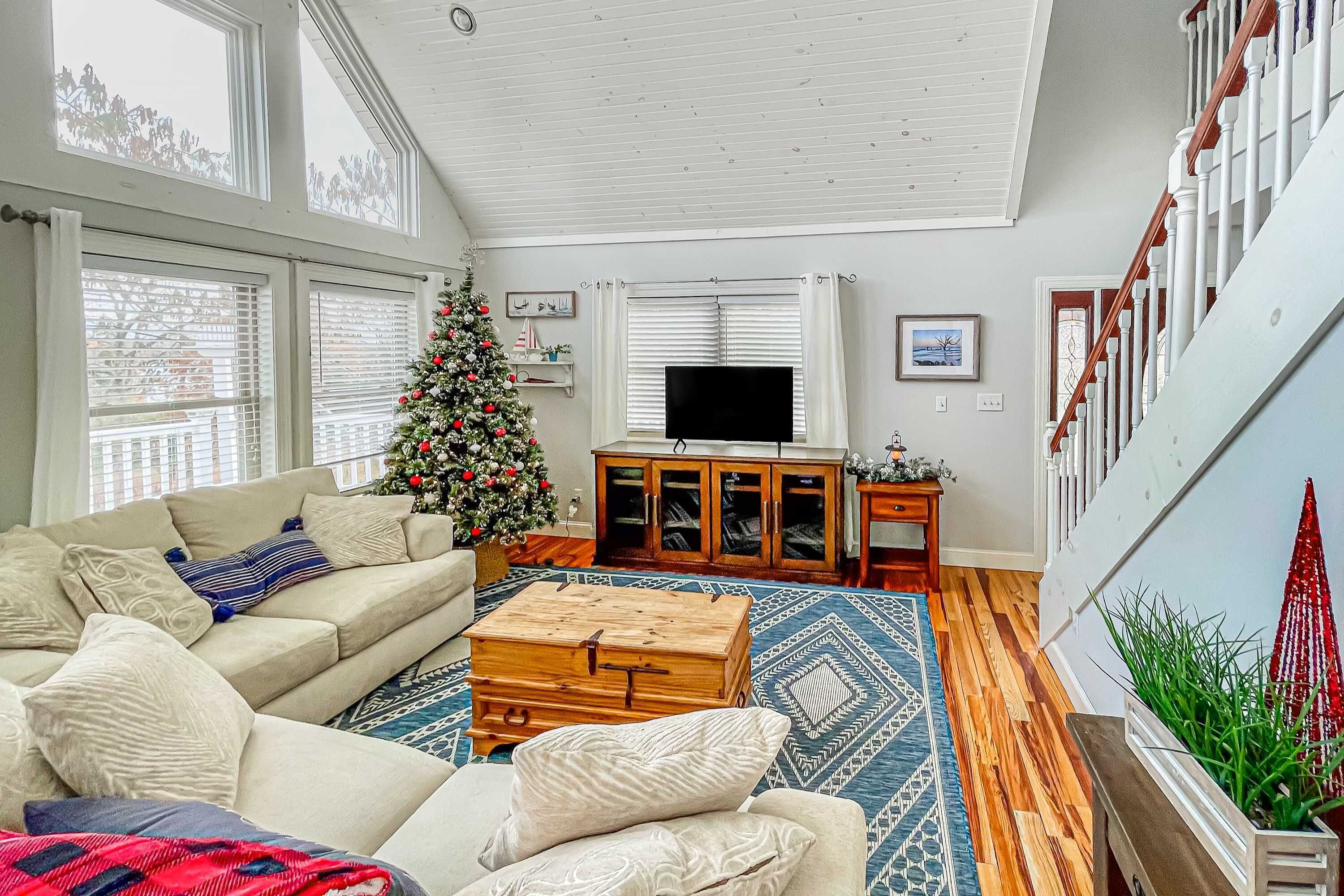 Uma sala de estar com uma janela grande, um armário de madeira, uma televisão e um pinheiro de Natal.