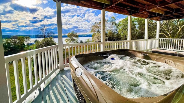 Un jacuzzi bajo una terraza de madera con vistas a un lago y montañas.