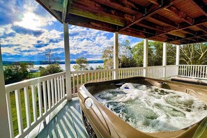 Een hottub onder een houten terras, met uitzicht op een meer en bergen.