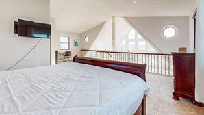 Un dormitorio con una cama grande, un televisor montado en la pared, un escritorio y vistas al exterior a través de una ventana.